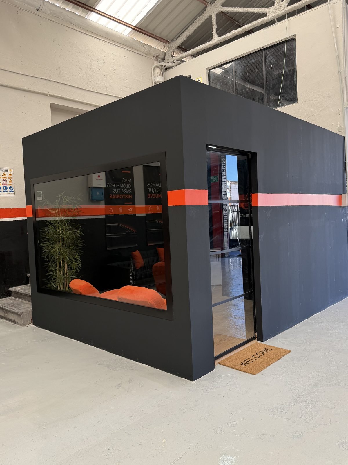 Sala de espera acristalada de Fast Cambio en Málaga: cabina de cristal con sofás de piel, sillones e iluminación cálida, con vista al taller.
